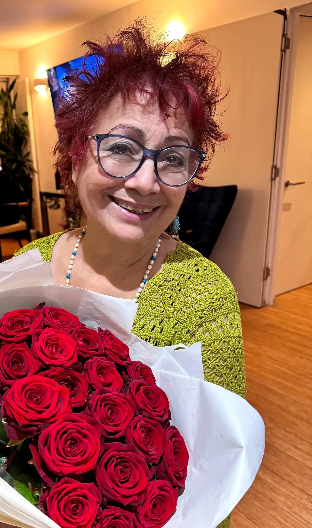 Anahita Eastwood in a green crocheted top and glasses, laughing, holding a large bouquet of red roses