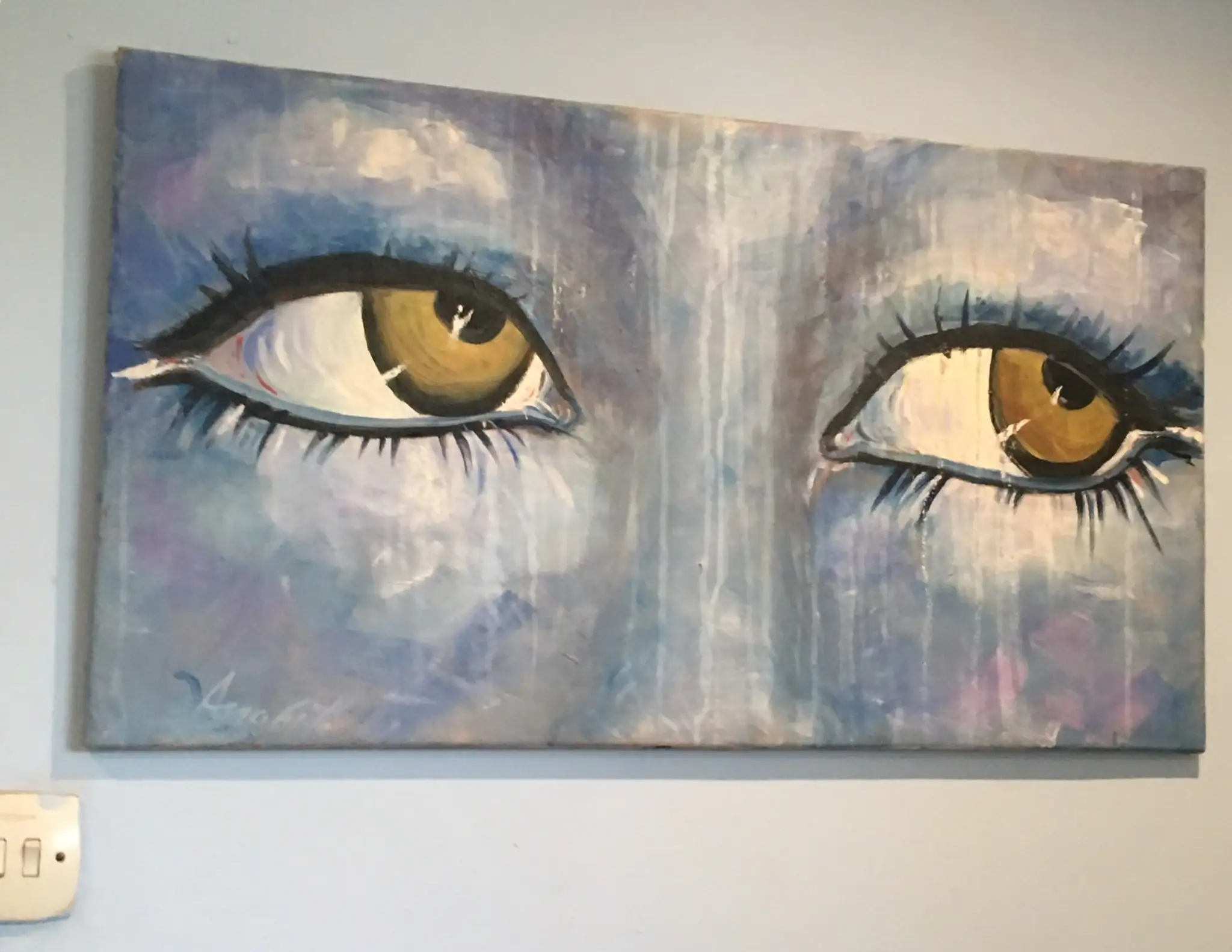 A wide painting of two amber-gold eyes with long dark lashes emerging from a wet-looking ground of blues, mauves and dripping whites