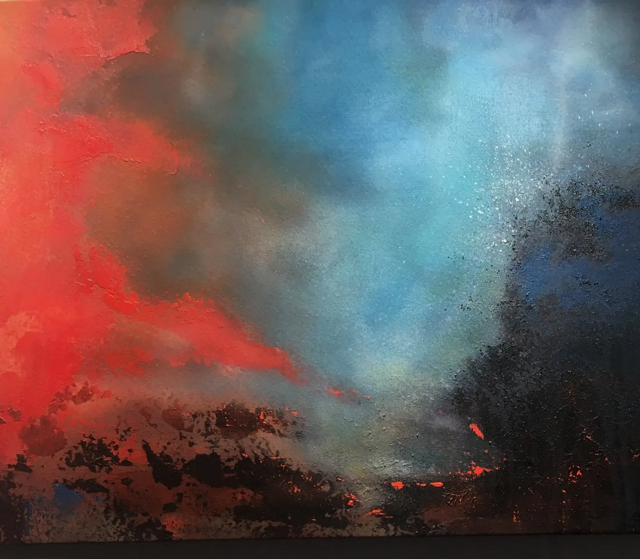 A wide sky painting: hot vermilion cloud on the left meets a cool turquoise blue on the right, with a dark, spattered treeline along the base and small speckles of red light glowing through the horizon.