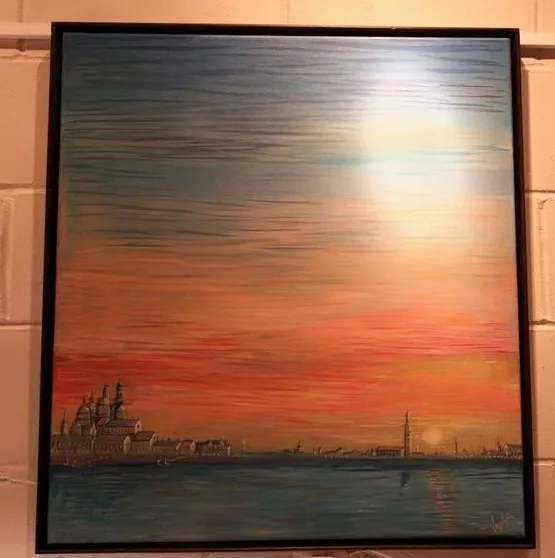 A wide bay at sunset with a Venetian-style skyline of domes, campanile and low waterfront buildings, under a teal sky graduating to orange with a bright column of light on the water