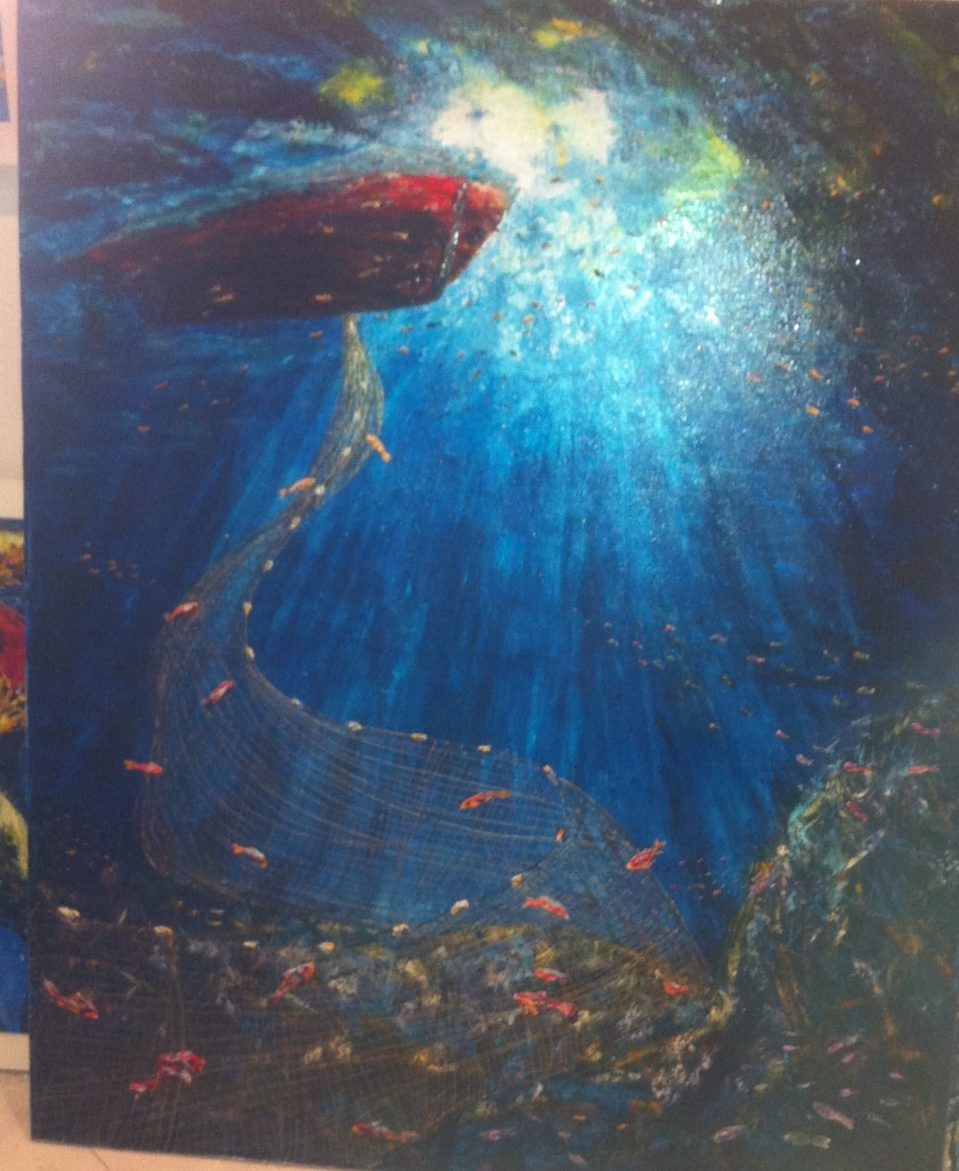 Underwater view in deep blue with a dark red boat at the surface, shafts of sunlight breaking through, a fishing net curving down and small bright fish drifting past.