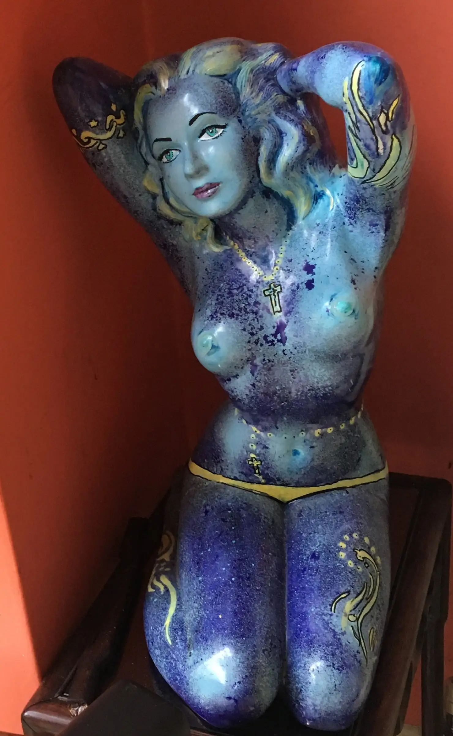 Glazed ceramic torso of a kneeling nude figure in cobalt and lapis with pale blue skin, blonde flowing hair, red lips, a small gold cross at the neck and fine gold linework across shoulders and thighs.