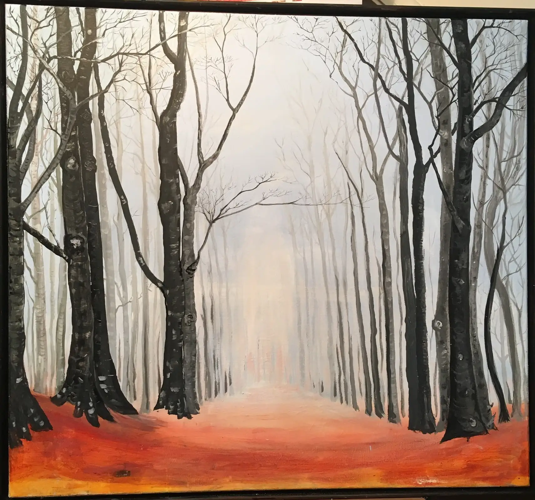 A tall corridor of leafless silver birches recedes into pale grey mist above a warm carpet of orange and red autumn leaves, in a slim black frame