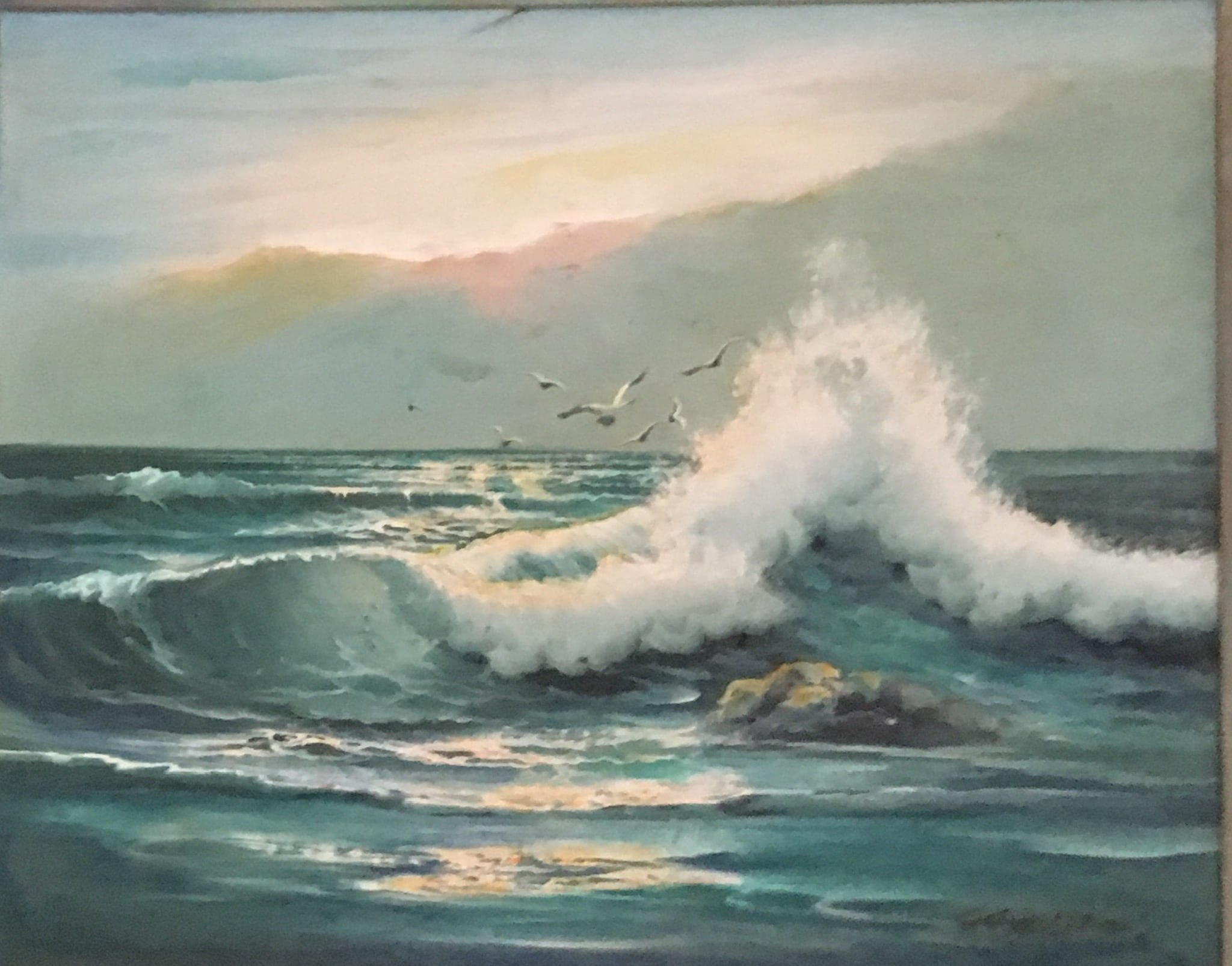 A tall cresting wave breaks in white spray over deep teal water at sunset, gulls wheeling above, a low rock catching warm light, soft peach and lilac sky behind.
