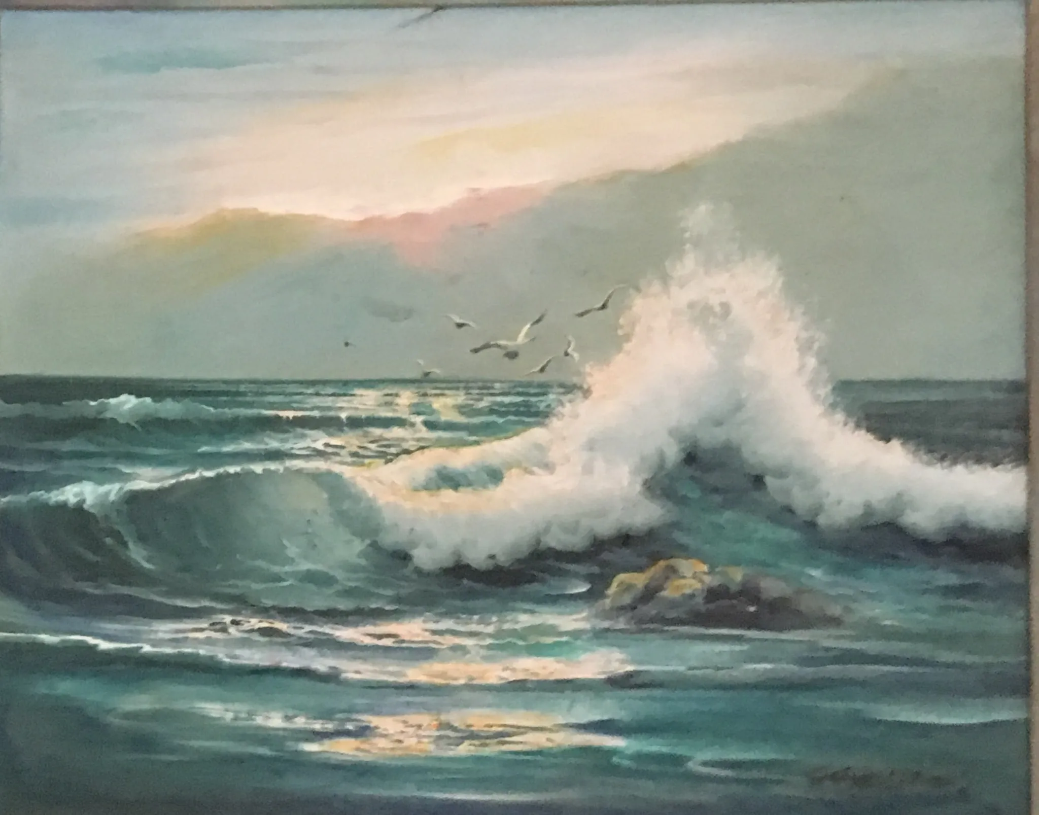 A tall cresting wave breaks in white spray over deep teal water at sunset, gulls wheeling above, a low rock catching warm light, soft peach and lilac sky behind.