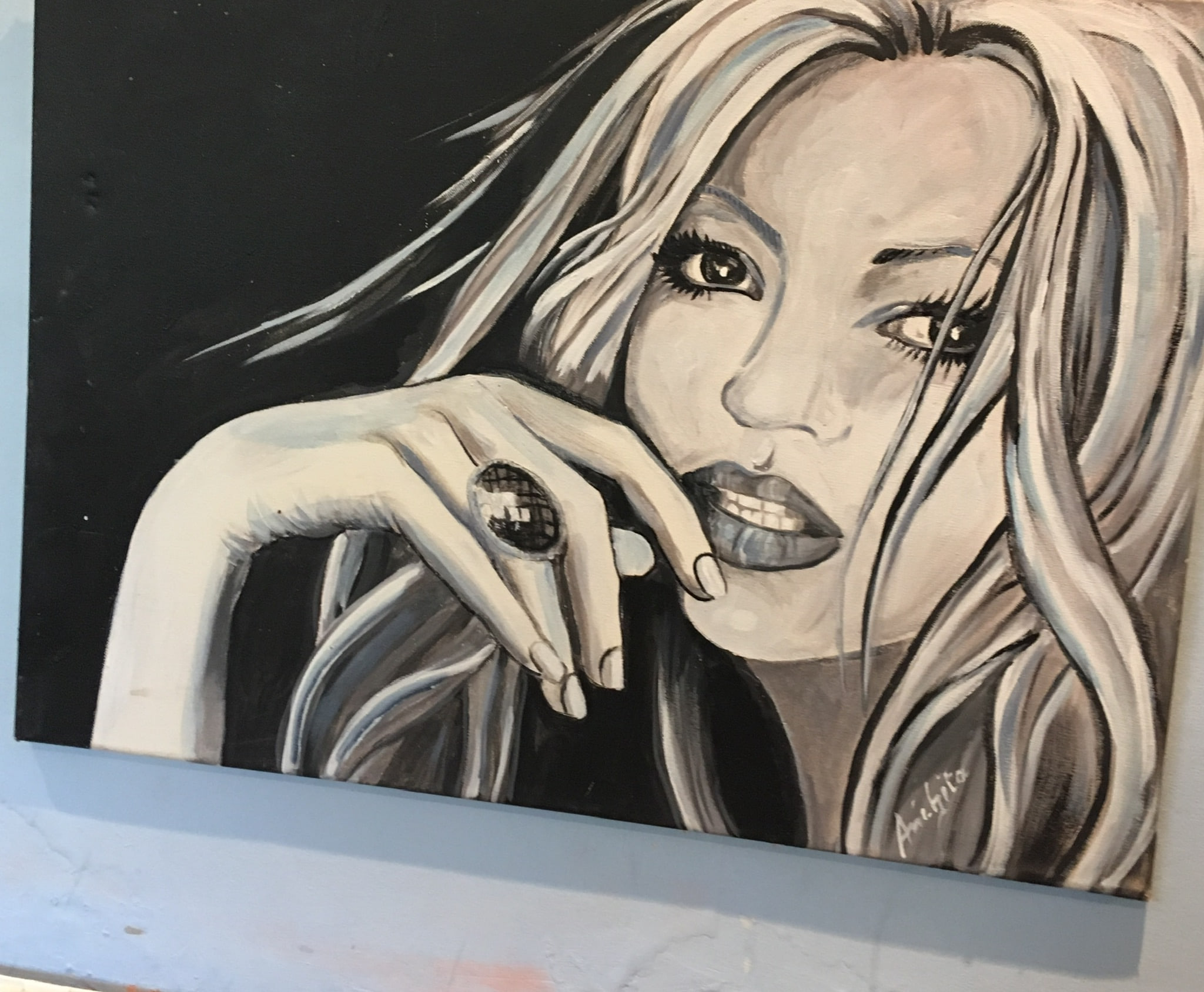 A close portrait of a young woman with long pale hair against black, her hand near her mouth with a large dark ring, painted in whites, greys and cool blue-black