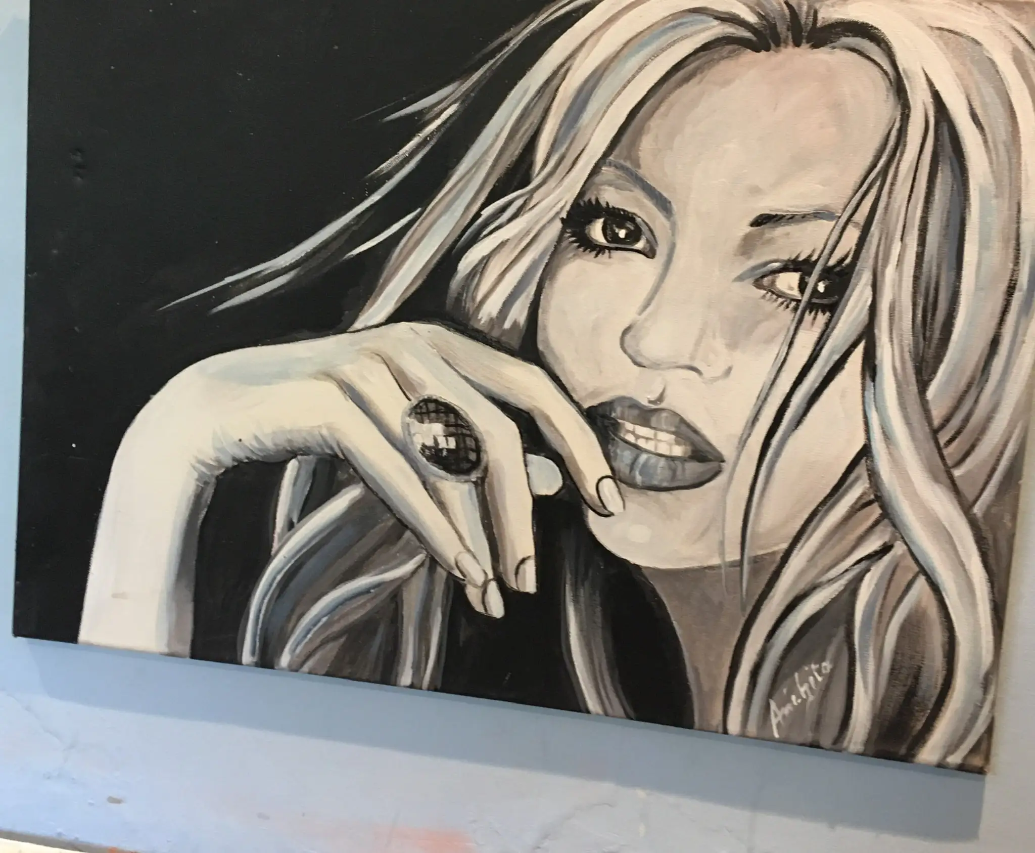 A close portrait of a young woman with long pale hair against black, her hand near her mouth with a large dark ring, painted in whites, greys and cool blue-black