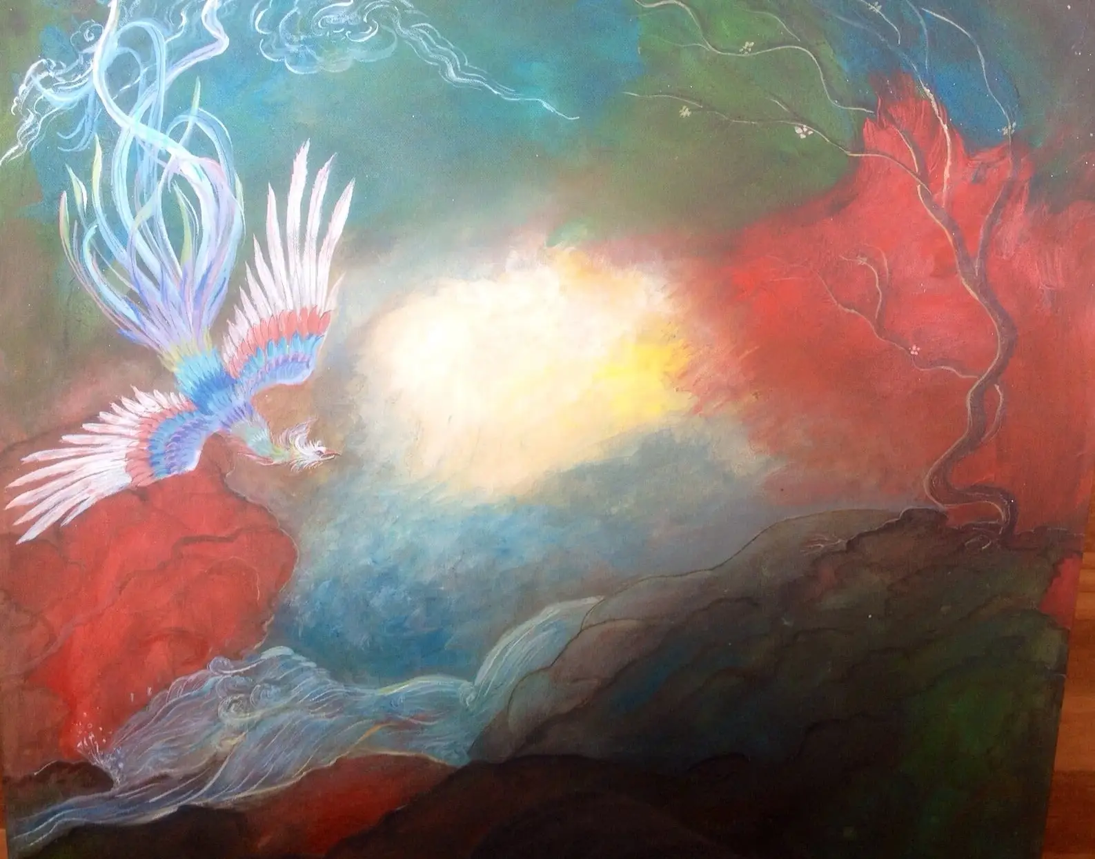 A phone-screen photograph of a similar phoenix landscape, the bird banking over red rocky hills under drifting white cloud with a soft glowing light at the heart of the sky