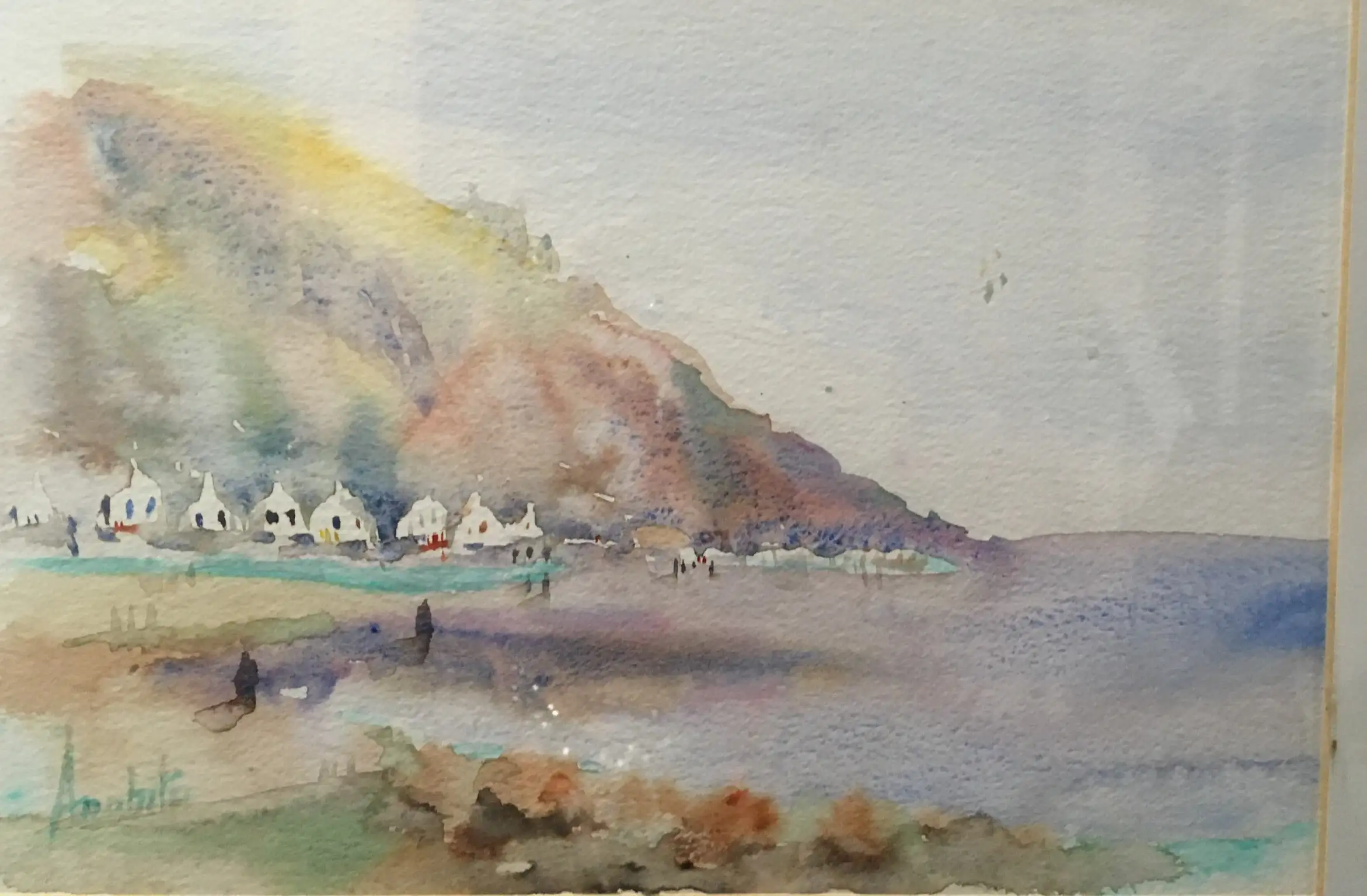 A watercolour of a small coastal village of whitewashed houses set at the foot of a tall pale cliff, with soft washes of yellow, mauve and blue running down to a wet sandy beach.