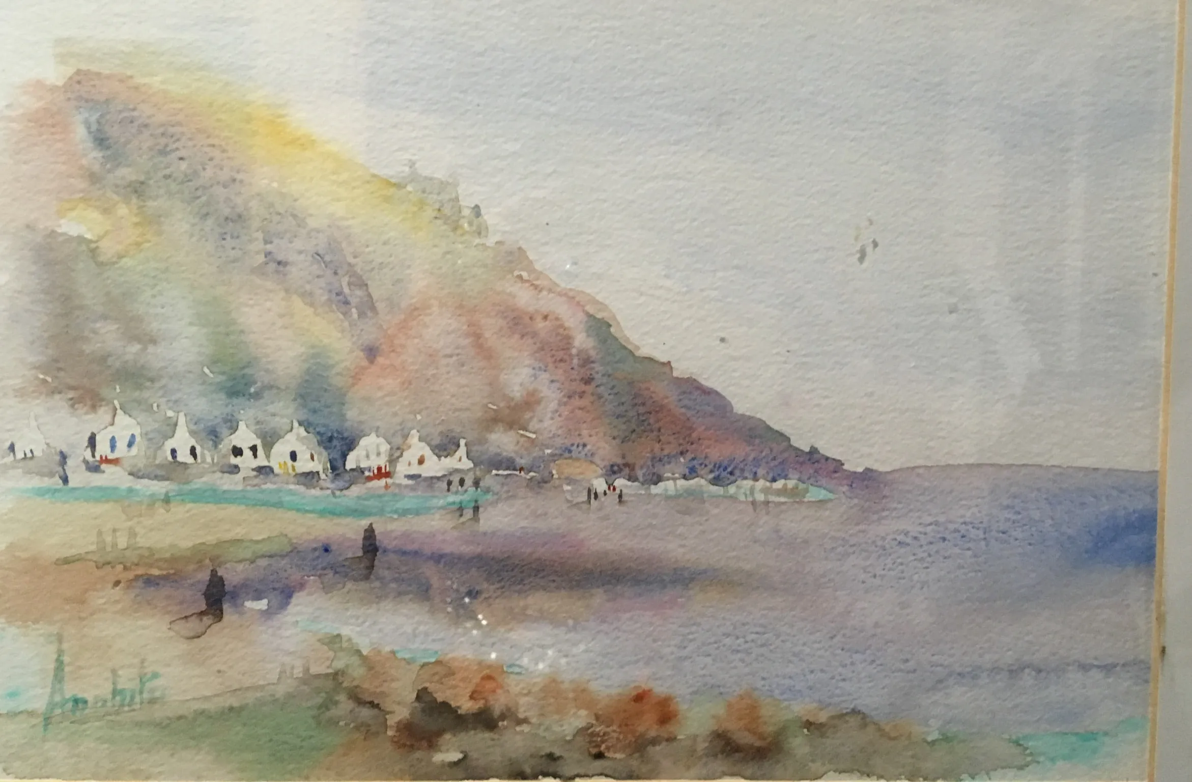 A watercolour of a small coastal village of whitewashed houses set at the foot of a tall pale cliff, with soft washes of yellow, mauve and blue running down to a wet sandy beach.